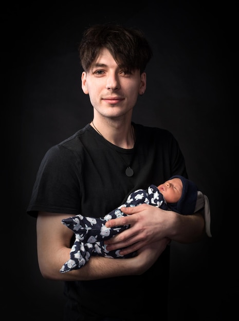 Jeune père et son petit garçon nouveau-né qui pose en studio sur fond noir