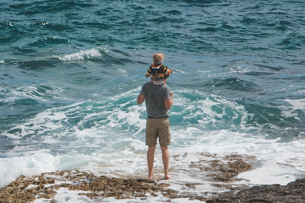 Jeune père tenant un enfant sur les épaules marchant au bord de la mer
