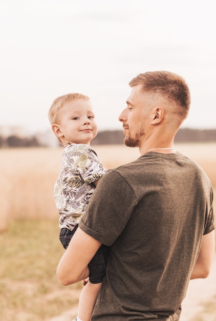 Un jeune père tient son fils dans ses bras et le regarde avec tendresse en été dans la nature.