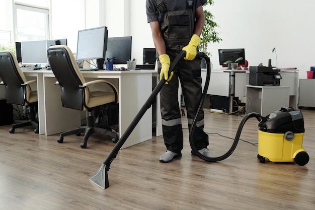 Jeune personnel masculin de l'entreprise de nettoyage en uniforme noir et gants jaunes