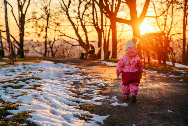 Jeune petite fille marchant dans le parc de la ville au coucher du soleil. vue de derrière. jouer dehors