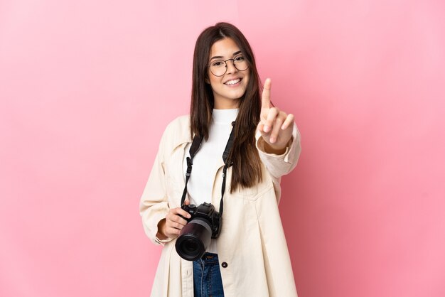 Jeune photographe brésilienne fille isolée sur un mur rose montrant et soulevant un doigt