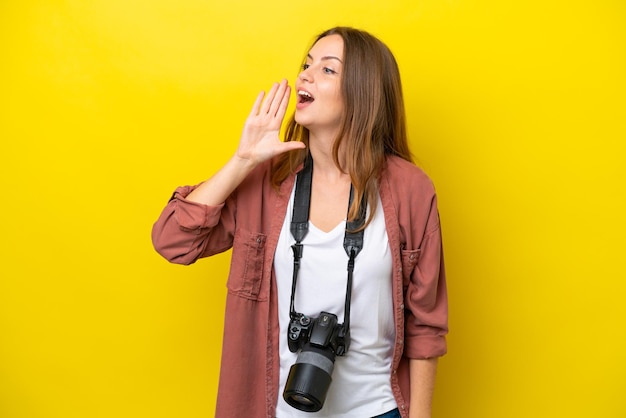 Jeune photographe caucasien femme isolée sur fond jaune criant avec la bouche grande ouverte sur le latéral