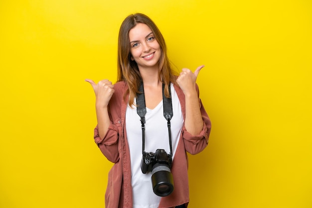 Jeune photographe caucasien femme isolée sur fond jaune avec le geste du pouce levé et souriant