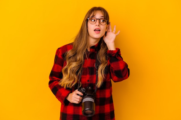 Jeune photographe caucasien femme isolée sur mur jaune en essayant d'écouter un potin