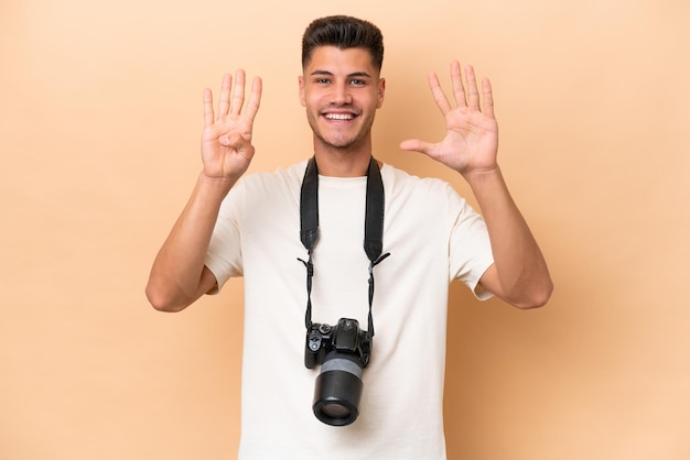 Jeune photographe caucasien homme isolé sur fond beige comptant neuf avec les doigts