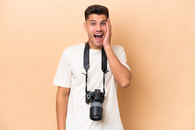 Jeune photographe caucasien homme isolé sur fond beige avec une expression faciale surprise et choquée