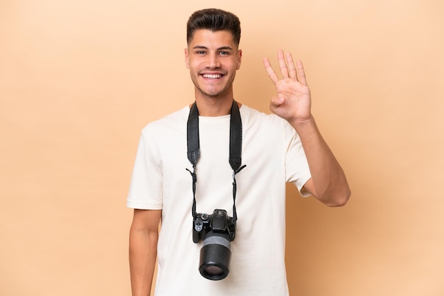 Jeune photographe caucasien homme isolé sur fond beige heureux et comptant quatre avec les doigts