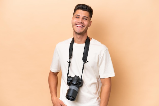 Jeune photographe caucasien homme isolé sur fond beige en riant