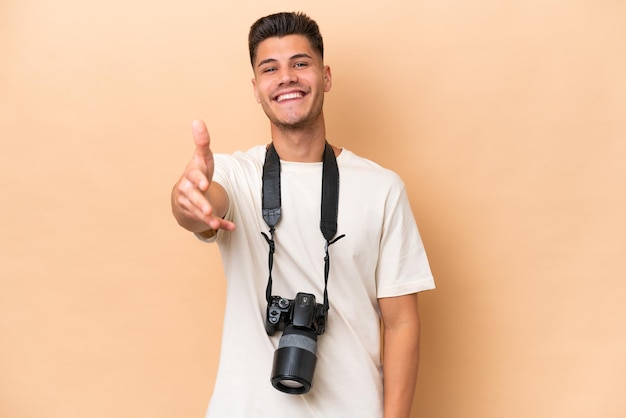 Jeune photographe caucasien homme isolé sur fond beige se serrant la main pour conclure une bonne affaire