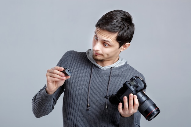 Un jeune photographe en chemise installe l'appareil photo. guy apprend à photographier sur fond gris