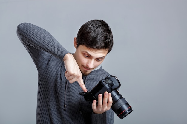 Un jeune photographe en chemise installe l'appareil photo. guy apprend à photographier sur fond gris