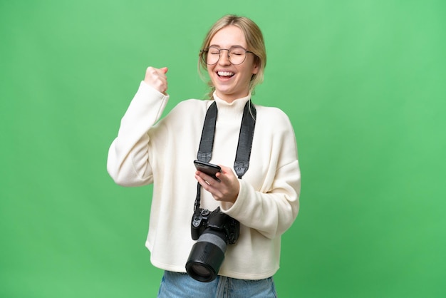 Jeune photographe femme anglaise sur fond isolé avec téléphone en position de victoire