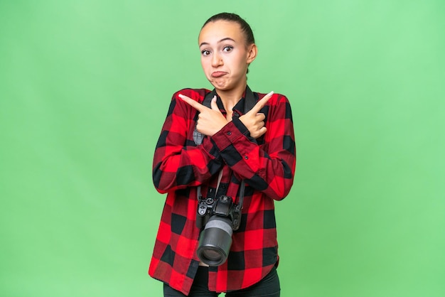 Jeune photographe femme arabe sur fond isolé pointant vers les latéraux ayant des doutes