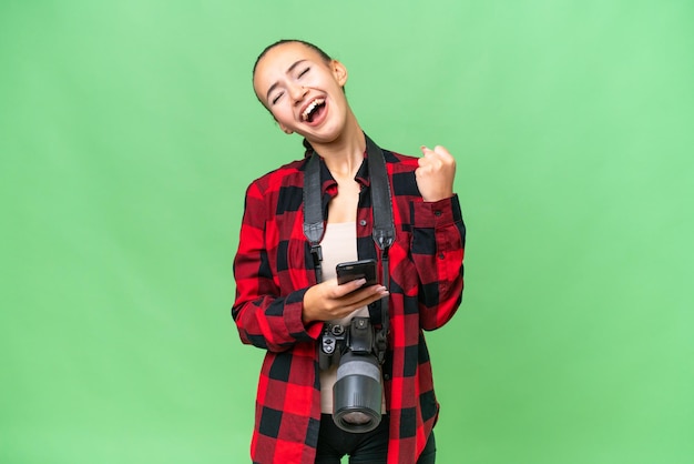 Jeune photographe femme arabe sur fond isolé avec téléphone en position de victoire