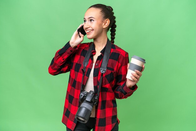 Jeune photographe femme arabe sur fond isolé tenant du café à emporter et un mobile