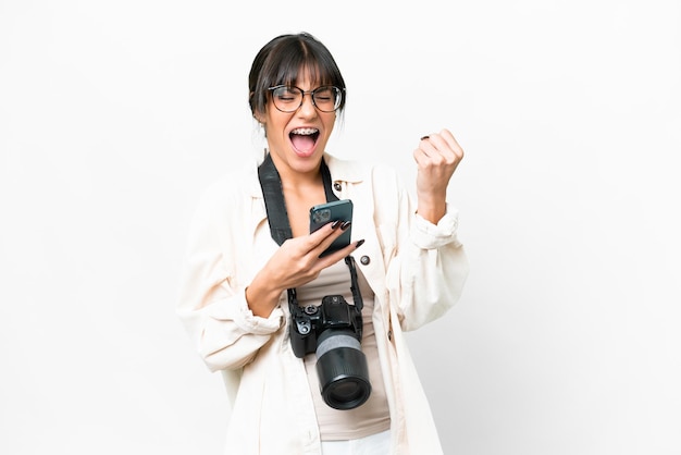 Jeune photographe femme caucasienne sur fond blanc isolé avec téléphone en position de victoire