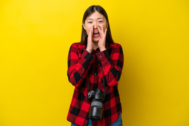 Jeune photographe femme chinoise isolée sur fond jaune criant et annonçant quelque chose