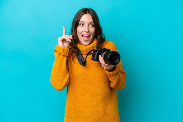 Jeune photographe femme isolée sur fond bleu ayant l'intention de réaliser la solution tout en levant un doigt