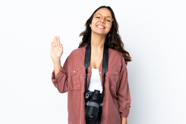 Jeune photographe femme sur mur blanc isolé saluant avec la main avec une expression heureuse