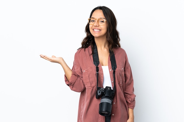 Jeune photographe femme sur mur blanc isolé tenant copyspace imaginaire sur la paume pour insérer une annonce