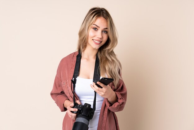 Photo jeune photographe fille sur mur isolé en envoyant un message avec le mobile