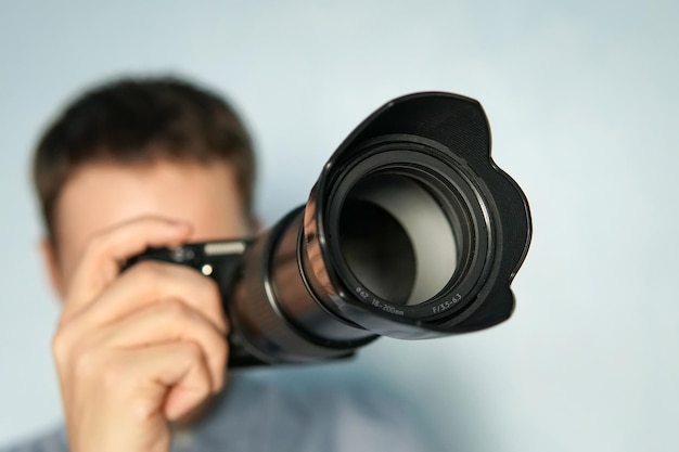 Jeune photographe sur fond bleu. Appareil photo sans miroir se bouchent dans la main d'un jeune homme sur fond bleu. Le journaliste prend une photo. le photographe regarde dans l'appareil photo. fermer