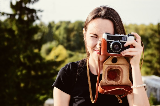 Jeune photographe heureuse se promène dans le parc avec appareil photo rétro