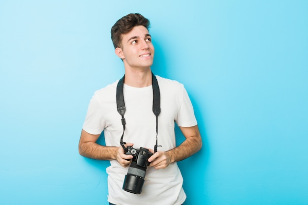 Jeune photographe homme tenant un appareil photo souriant confiant avec les bras croisés