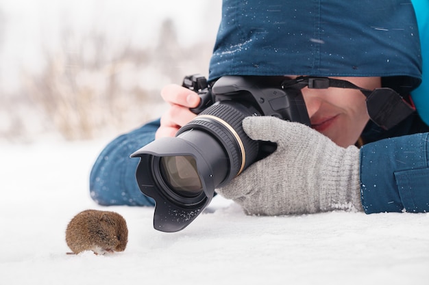 Photo jeune photographe prenant des photos macro d'une souris en bois sur la neige