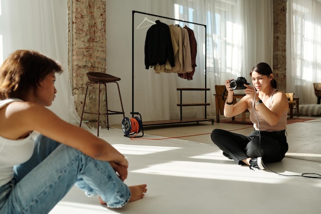 Jeune photographe professionnel assis sur le sol d'un studio spacieux et ensoleillé