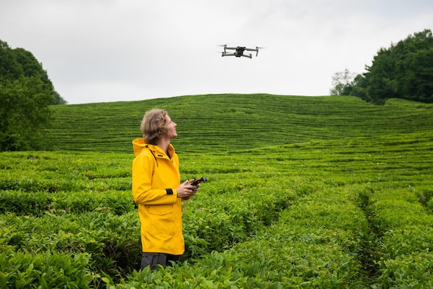 Un jeune photographe se tient dans un champ de thé vert et prend des photos aériennes avec un drone