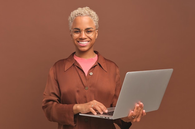 Une jeune pigiste afro-américaine heureuse tient un ordinateur portable ouvert et sourit