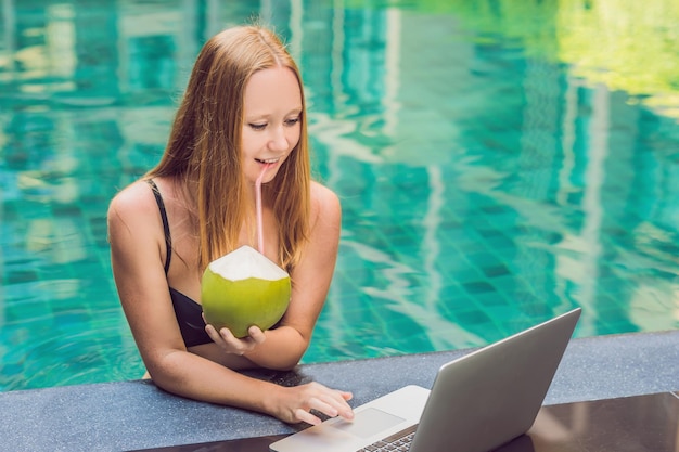 Jeune pigiste assise près de la piscine avec son ordinateur portable. Occupé pendant les vacances. Concept de travail à distance. Copiez l'espace pour votre texte