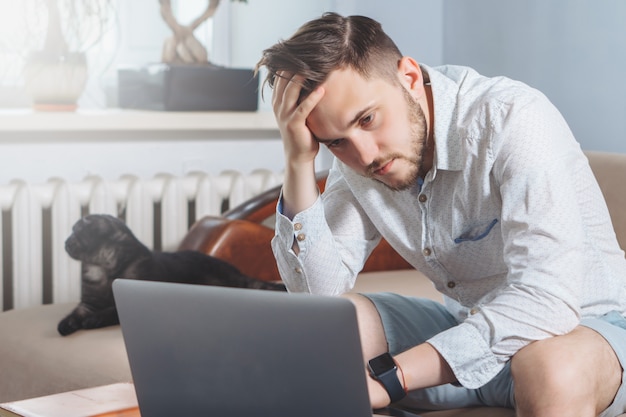 Jeune pigiste fatigué à l'aide d'un ordinateur portable tout en travaillant à domicile