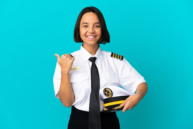 Jeune pilote d'avion sur fond bleu isolé pointant vers le côté pour présenter un produit