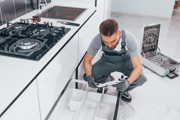 Jeune plombier professionnel en uniforme gris travaillant dans la cuisine