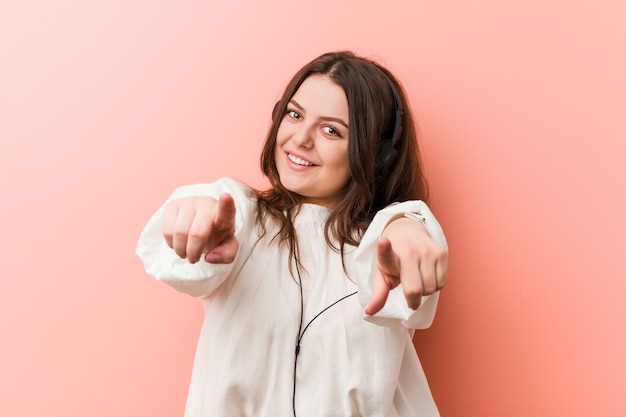 Jeune, plus la taille de femme écoutant de la musique avec casque sourit joyeux pointant vers l&#39;avant.