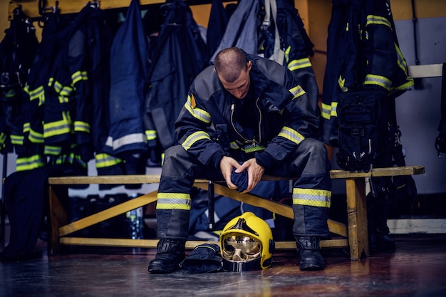 Jeune pompier attrayant en uniforme de protection assis dans la caserne des pompiers.