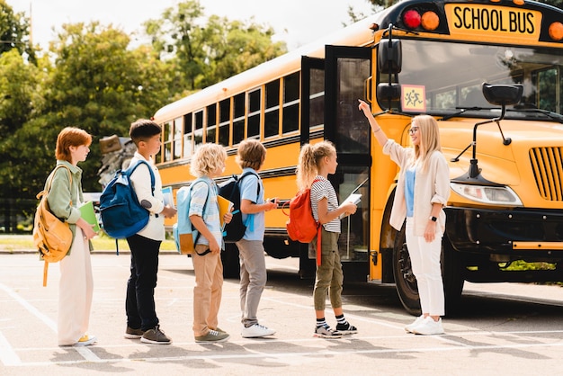 Jeune professeur comptant un groupe d'enfants élèves écoliers avant de monter dans le bus scolaire avant les leçons Bienvenue à l'école après les vacances d'été Nouveau semestre de l'année scolaire