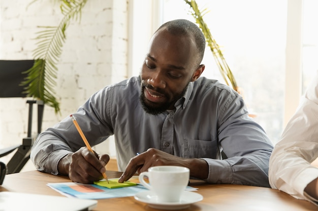 Jeune professionnel des affaires se préparant à une réunion dans un bureau de création. L'homme d'affaires écrit de nouvelles décisions, des plans futurs et une stratégie. Réunion et lieu de travail créatifs, affaires, finances, travail d'équipe.