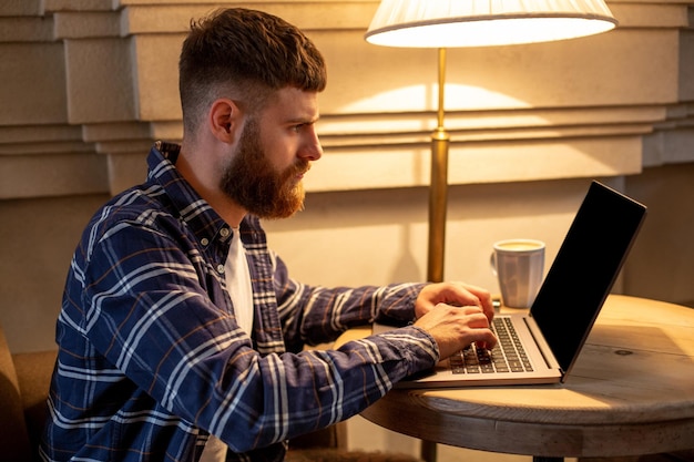 Jeune professionnel surfant sur Internet sur son ordinateur portable avec une tasse de café sur une table au café ou au bureau à domicile, travaillant à partir du concept de café