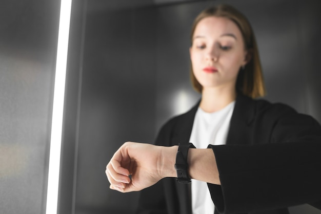 Jeune professionnelle vérifiant sa montre dans l'ascenseur.