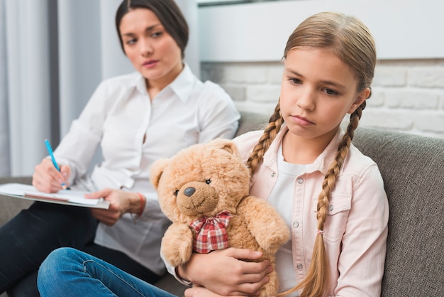 Photo jeune psychologue observant la fille triste assise avec ours en peluche