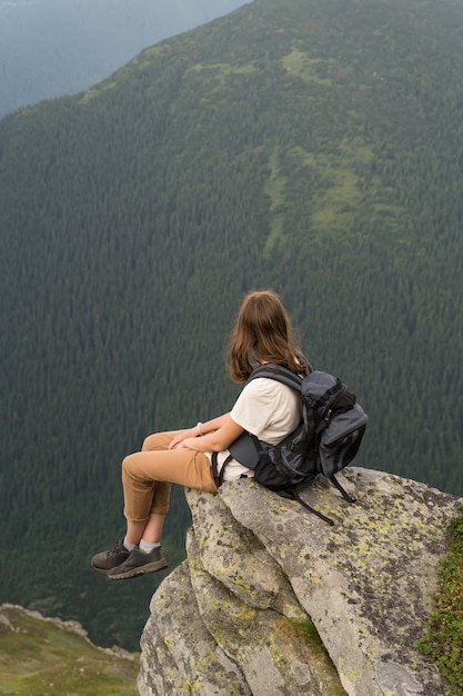 Jeune randonneur jeune femme repose sur une falaise et profite d'un paysage à couper le souffle de montagnes couvertes de forêts de pins