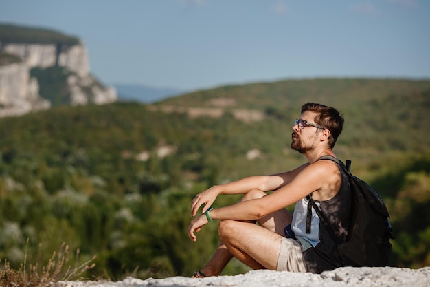 Jeune randonneur avec sac à dos relaxant au sommet d'une montagne pendant le calme coucher de soleil d'été