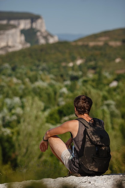 Jeune randonneur avec sac à dos relaxant au sommet d'une montagne pendant le calme coucher de soleil d'été