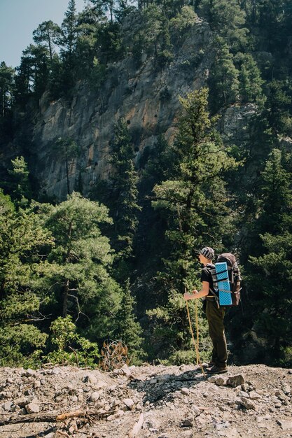 Jeune randonneur sportif masculin trekking avec sac à dos dans les montagnes au-dessus d'une forêt sombre avec de grands pins. Concept de sport et de vie active.