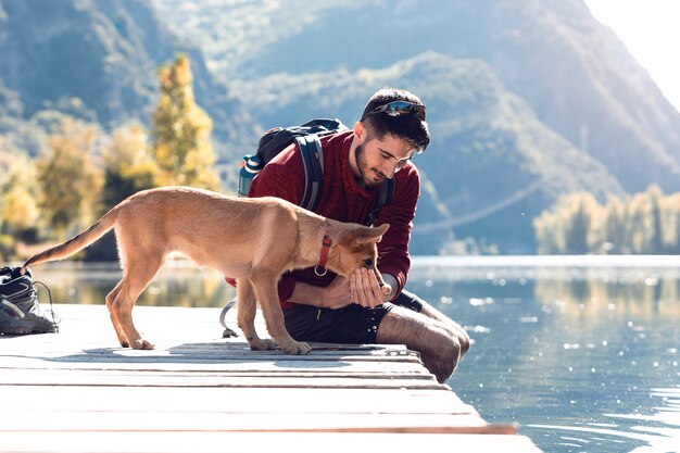 Jeune randonneur voyageur avec sac à dos donnant de l'eau au chien sur le lac.