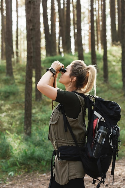 Jeune randonneuse utilise des jumelles pour observer les oiseaux dans la forêt verte